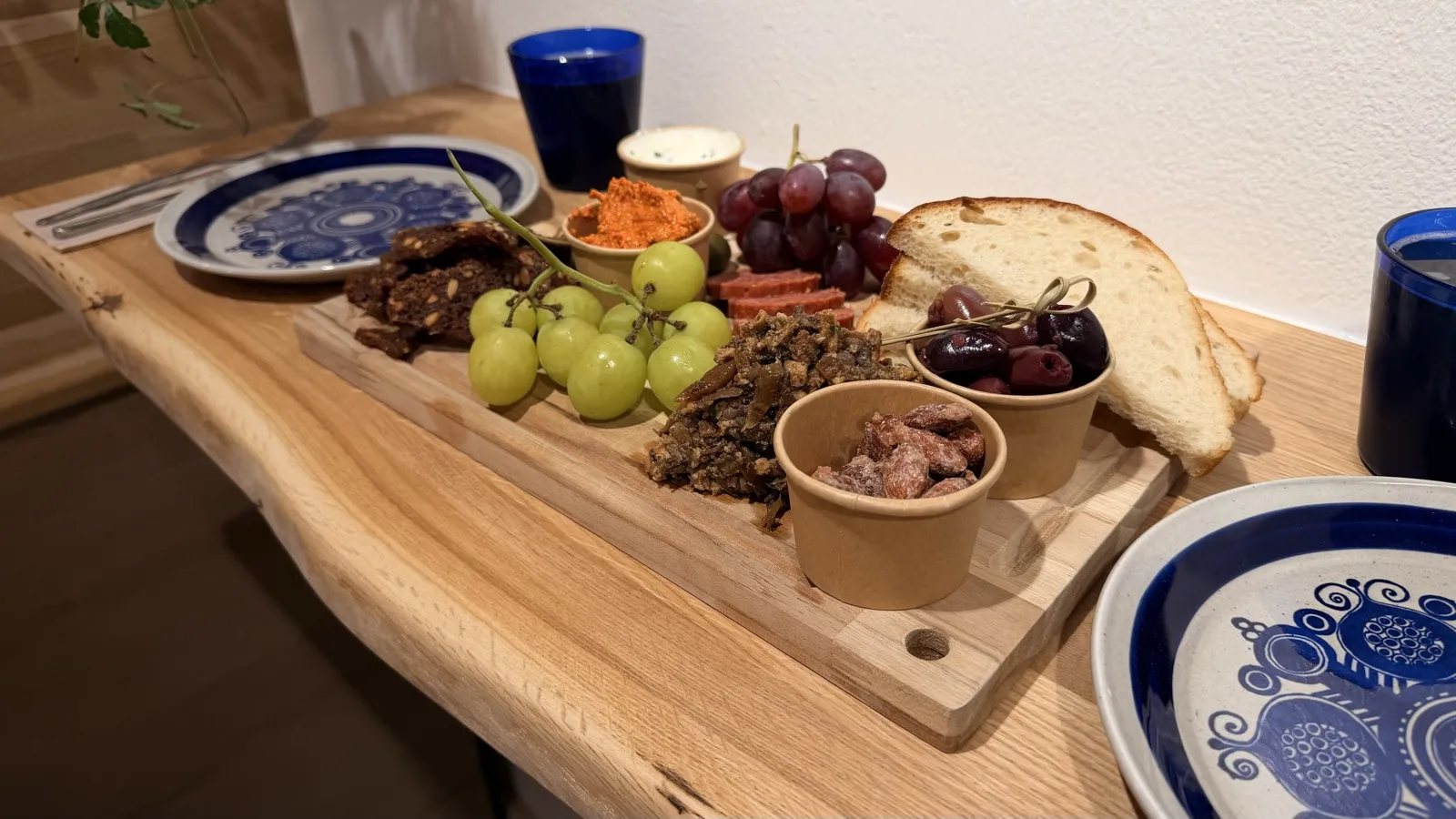 Sloppy Tapasbræt on a wooden board: grapes, olives, almonds, romesco, rye bread crisps, "chorizo" and bread