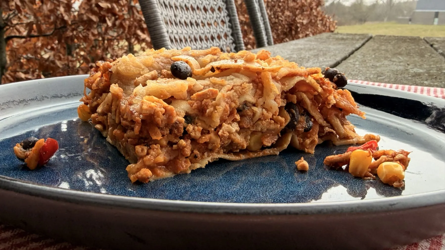 Et stykke Mexi Lasagne på en dybblå tallerken, lag af pasta, bønner, majs og gyldent fyld tydeligt synlige